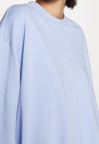 T-shirt in cotone oversize azzurro chiaro con scollo tondo, spalle basse e texture liscia, con tessuto leggermente stropicciato visibile.