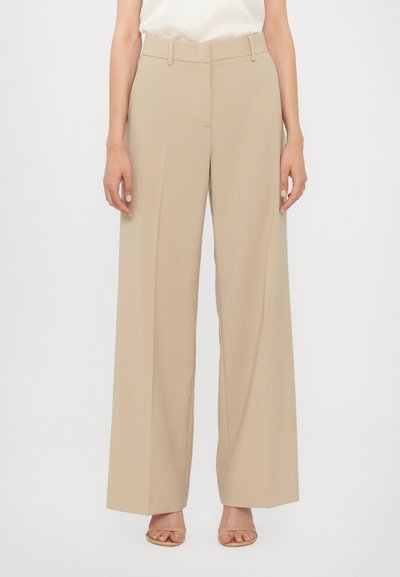 Pantalons larges beiges avec une coupe ajustée, fabriqués en tissu lisse. Présentent une taille plate, des passants de ceinture et un pli subtil le long des jambes.