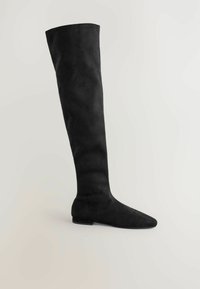 Schwarze Wildleder-Stiefel �über das Knie mit spitzem Zehenbereich und niedrigem Absatz vor einem schlichten hellen Hintergrund.