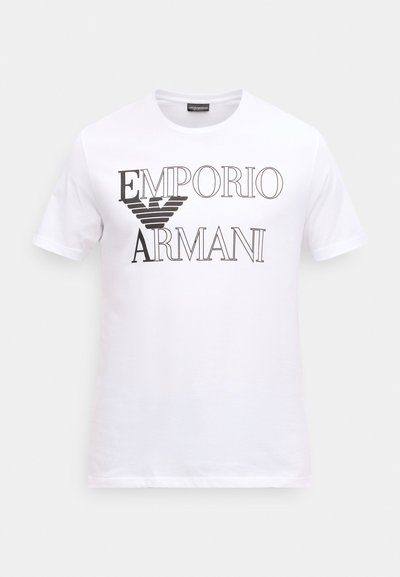 Balta kokvilnas T-krekls ar uzrakstu "EMPORIO ARMANI" melniem bold burtiem, centrā stilizēts ērglis. Īsas piedurknes, klasiskā piegriezuma.
