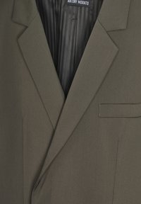 Blazer verde oliva con rever a punta, tasca sul petto, e rivestimento a righe nere, realizzato in tessuto liscio con una vestibilità su misura.