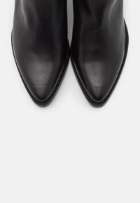 Paire de bottes pointues en cuir noir vues de dessus sur un fond clair uni.