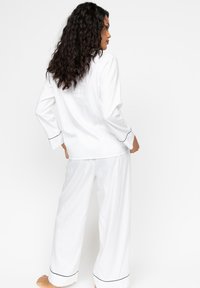 Witte pyjama set met lange mouwen en losse broek met marineblauwe piping accenten. Zacht, glad materiaal met een ontspannen pasvorm.