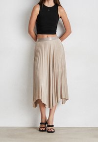 Gonna midi plissettata beige con una cintura lucida; abbinata a un top aderente nero e sandali neri con lacci. Tessuto morbido con un design fluido.