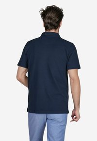 Marineblauwe polo gemaakt van katoen, met een klassieke kraag, korte mouwen en een rechte zoom. Geweven stof met minimale details.