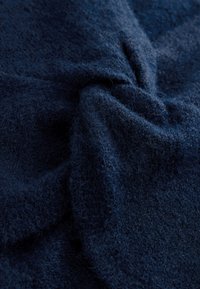 Tissu en laine bleu foncé avec une texture douce et duveteuse, présenté en gros plan avec des plis naturels et des fibres visibles.