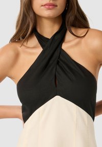 Svart og kremfarget halterneck-kjole med krysshals og nøkkelhulldetalj, som har en jevn tekstur og en tettsittende design.