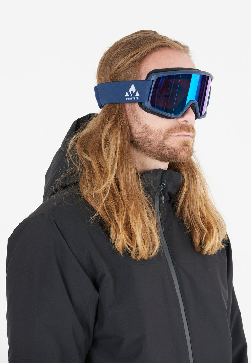 Skidglasögon med ett mörkblått band och reflekterande linser. Har en svart ram och en logotyp på remmen. Bärs av en individ i en svart jacka.