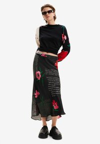 Gonna nera floreale con motivo testuale, abbinata a un top lungo nero e colorato e a scarpe piattaforma nere e chunky.