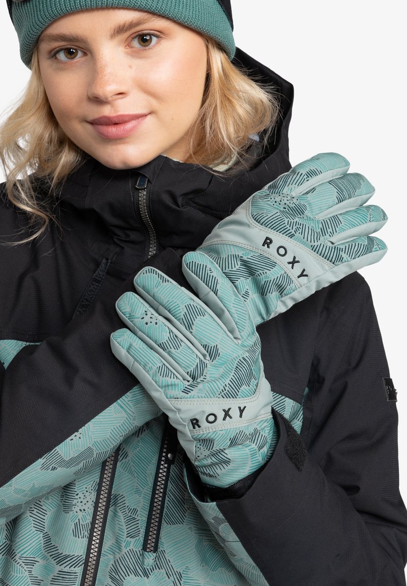 Light teal gloves with a geometric pattern, logo "ROXY" on the cuff, worn by a person in a black outer jacket with teal accents.