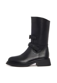 Botin de piele neagră, cu gleznă, având un șanț larg și structurat, două curele ajustabile, un vârf rotunjit și un toc modest tip bloc. Suprafață texturată.