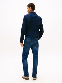 Suéter de punto trenzado en navy con un cuello alto, combinado con jeans azules. El modelo está de espaldas, mostrando la textura y el ajuste del suéter.