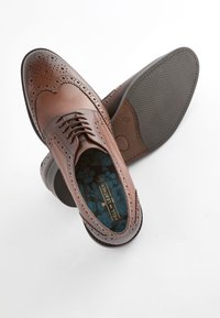 Brown leather dress shoes with brogue detailing, rounded toe, laces, and a textured rubber sole. Floral-patterned interior lining.