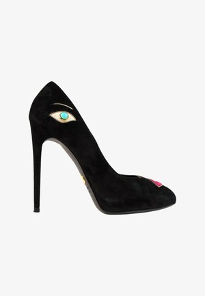 Chaussure noire à talon haut avec un motif œil turquoise près du talon et un détail de lèvres roses sur l'orteil, sur fond blanc.