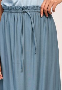 Jupe fluide bleu clair avec une taille élastique froncée et un lien réglable. Le tissu paraît lisse et léger.