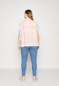 Overdimensjonert t-skjorte med korte ermer i lys rutete mønster med rosa og hvite toner, sammen med tettsittende blå jeans og lilla joggesko. Bakside.