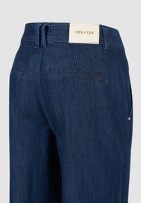 Jeans in denim scuro con vita media, dotati di un'etichetta con "YES ZEE", tasche posteriori e dettagli di cucitura sottili.