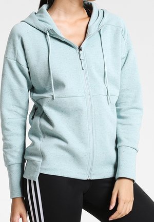 Vaaleansininen vetoketjullinen huppari, jossa on kiristysnyörit, päällä henkilö, jolla on mustat legginsit valkoisilla sivuraitoja, kuvattuna kaulasta lantioihin.