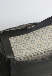 Schwarze Lederhandtasche mit einem gemusterten beigen Innenraum, der braune und hellblaue Sterne zeigt. Reißverschluss mit silberfarbener Hardware.
