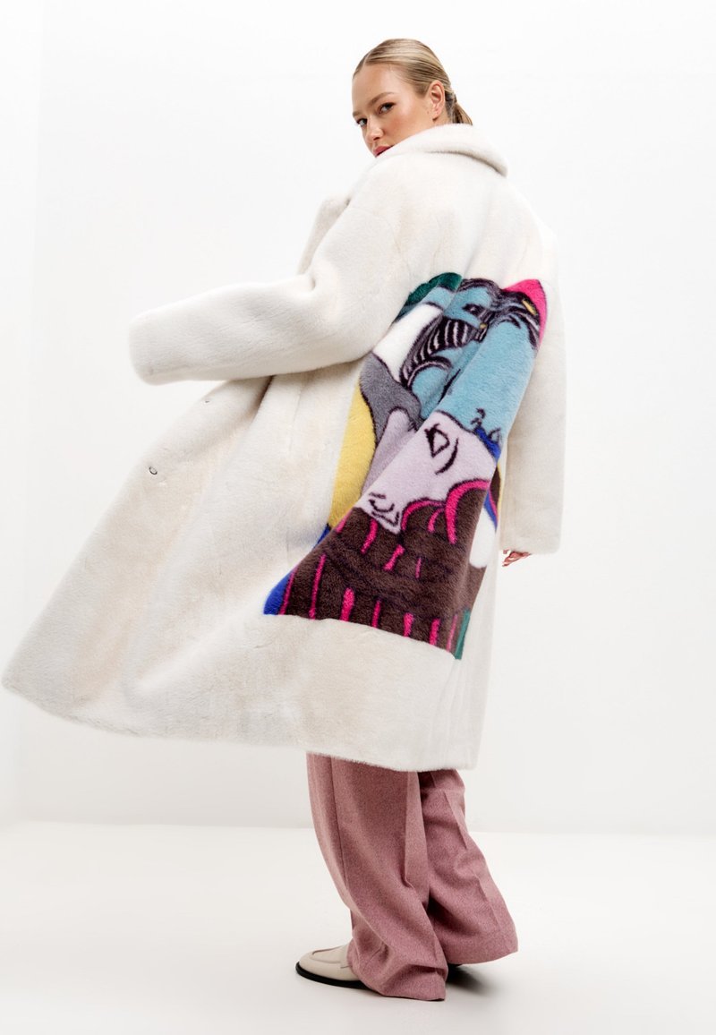 Vit faux fur-kappa med en stor, färgglad grafisk design på baksidan. Kappan har en bred krage och är något oversized.