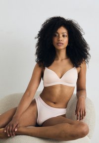 Ensemble de soutien-gorge et culotte assortis en rose pâle, fabriqué dans un tissu doux et lisse. Le soutien-gorge présente un décolleté plongeant et des bretelles ajustables.