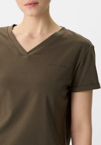 Olijfgroene V-hals t-shirt van zacht, lichtgewicht materiaal met opgerolde korte mouwen en subtiele geborduurde logodetails op de borst.