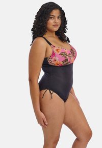 Dámský jednodílný plavky s květinovým růžovým a černým topem, s nastavitelnými ramínky a černým spodním dílem se bočními šňůrkami. Hladká textura celkově.