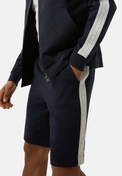 Marineblaue Shorts mit seitlichen Taschen, versehen mit einem strukturierten, hellgrauen Streifen und Branding. Hergestellt aus weichem, dehnbarem Stoff für zusätzlichen Komfort.