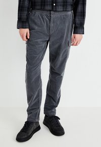 Grijze cargobroek met een elastische tailleband, gestructureerde stof, zijzakken en een losse pasvorm. Gekoppeld aan zwarte sneakers.