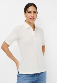 Polo skjorte i off-white, korte ærmer, med en knaplukning og en klassisk krave. Stoffet virker glat med en let glans.