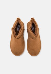Bottines en suede marron avec un intérieur doux et duveteux, dotées d'un bout arrondi et de détails cousus le long du bord. Deux anses sur les côtés.