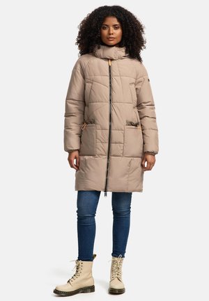 Veste matelassée beige avec un col montant, fermeture éclair sur le devant, deux poches avant et des accents en toggle ; associée à un jean bleu et des bottes beiges.
