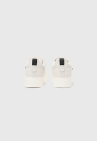 Baskets blanches avec un matériau lisse, présentant un panneau arrière texturé, une languette de talon noire et une épaisse semelle blanche. Design minimaliste.