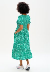 Grön leopardmönstrad klänning med korta puffärmar, smockad bodice, lager-skirt och sidofickor, kombinerad med vita och rosa sneakers.