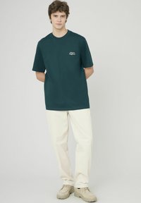 T-shirt en coton bleu canard à manches courtes, ornée d'un petit graphisme en texte blanc sur la poitrine, associée à un pantalon de couleur crème.