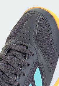 Grijze sportfiets met een gestructureerde bovenkant, turquoise accenten, oranje zool en grijze veters. Inclusief ventilatiegaten in de teen.