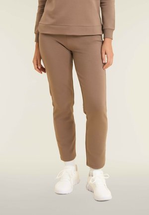 Joggers ajustés de couleur marron en tissu doux avec une texture lisse, associés à des baskets blanches et des chaussettes en coton arrivant à la cheville.