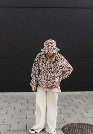 Kurtka polarowa i kapelusz typu bucket w panterkę, o miękkiej fakturze. Połączone z różową warstwą i szerokimi białymi spodniami na ciemnym tle.