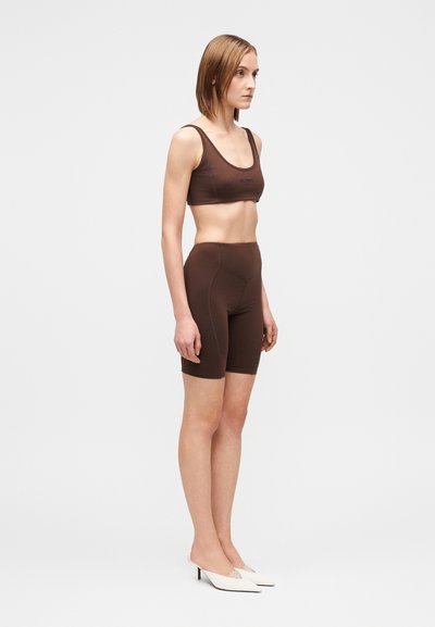 Conjunto de top deportivo marrón y shorts de cintura alta, hechos de material elástico y suave. Cuenta con un escote redondo y detalles sutiles de costura.