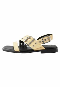 Sandală din piele galbenă, cu un bretele cu cataramă, decupaje circulare și o talpă plată neagră. Design deschis pentru respirabilitate și confort.