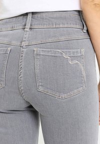Vaqueros gris denim de talle alto, con dos bolsillos traseros con un detalle sutil de costura y un diseño ajustado. Textura suave.
