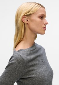 Gray knit sweater with a ribbed texture, round neckline, and soft finish. Features a small embroidered logo on the chest.