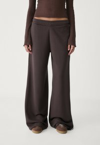 Wijde, donkerbruine sweatpants van zachte stof met een elastische tailleband. Gecombineerd met een getailleerde ribbeltop en casual sneakers.