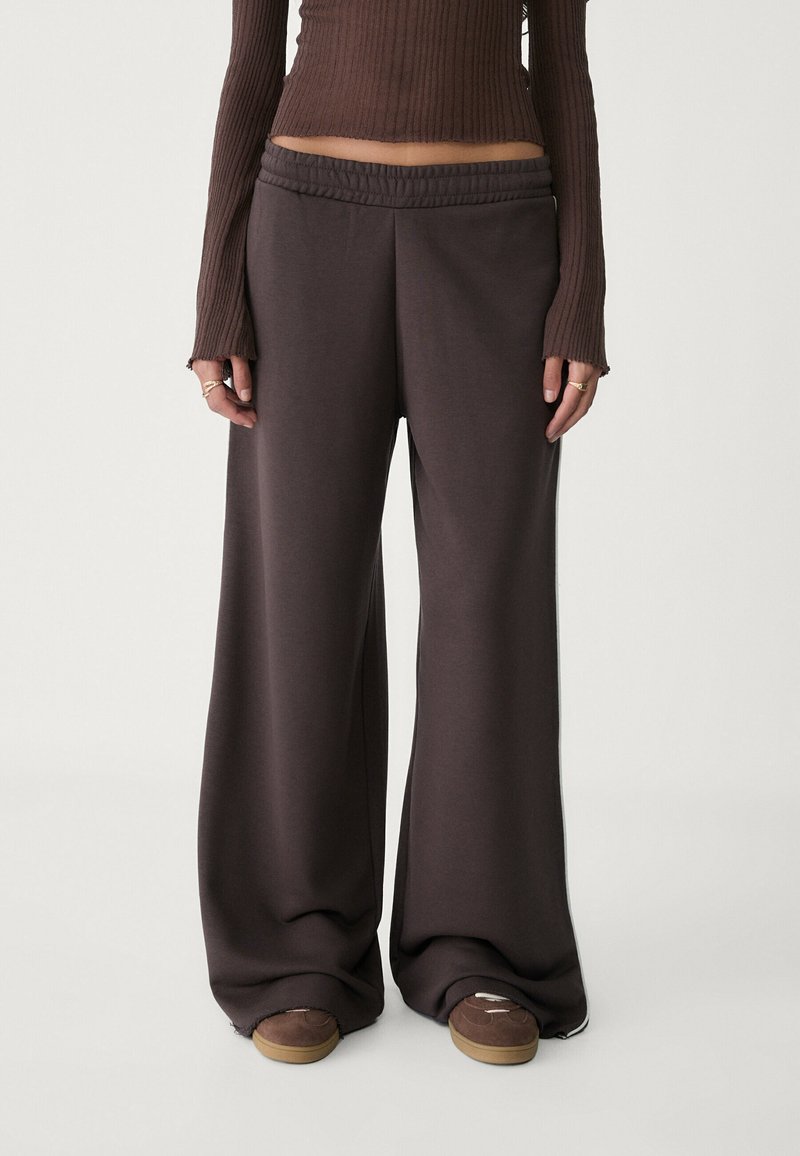 Wijde, donkerbruine sweatpants van zachte stof met een elastische tailleband. Gecombineerd met een getailleerde ribbeltop en casual sneakers.