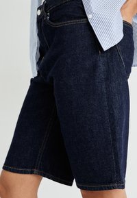Mørke denimshorts med rett snitt, med kontrastsøm og knappelukking. Synlige front- og sidelommer.