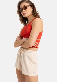 Red ribbed crop top paired with beige cotton shorts. The shorts feature an elastic waistband and pockets, with a small logo on the side.
