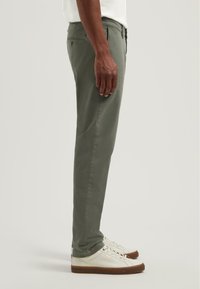 Zöld chinos nadrág, slim fit fazonnal, elülső és hátsó zsebekkel, fehér inggel és világos színű sportcipővel párosítva. Sima anyagtextúra.