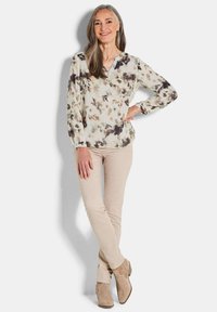 Blusa leggera a fantasia floreale in crema, grigio e marrone scuro con scollo a v e dettagli di bottoni, abbinata a pantaloni beige aderenti e stivaletti color cammello.
