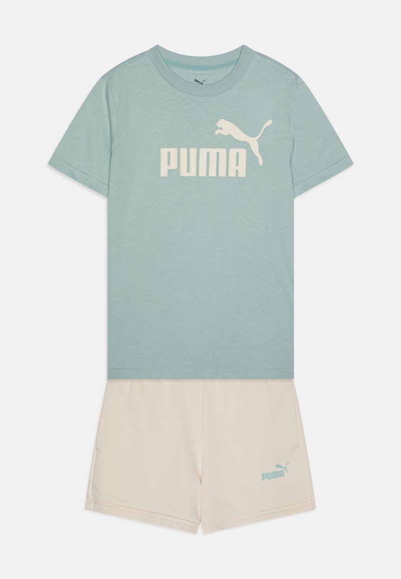 Camiseta azul claro con el logo "PUMA" en blanco; combinada con pantalones cortos crema que cuentan con un pequeño logo "PUMA" en azul. Material de algodón, diseño casual.