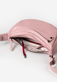 Lichtroze leren tas met een ritsluiting, voorzien van een rode binnenzak en een afneembare schouderband. Soepele textuur, minimalistisch ontwerp.